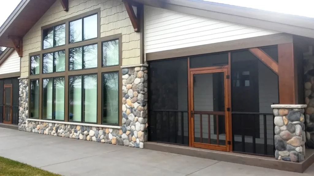 Modern house exterior with large windows, stone accents, and a screened porch with a wooden door.