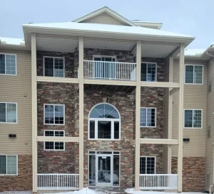 commercial-10 Three-story apartment building with stone and beige siding, large entryway, balconies, and snow on the ground.