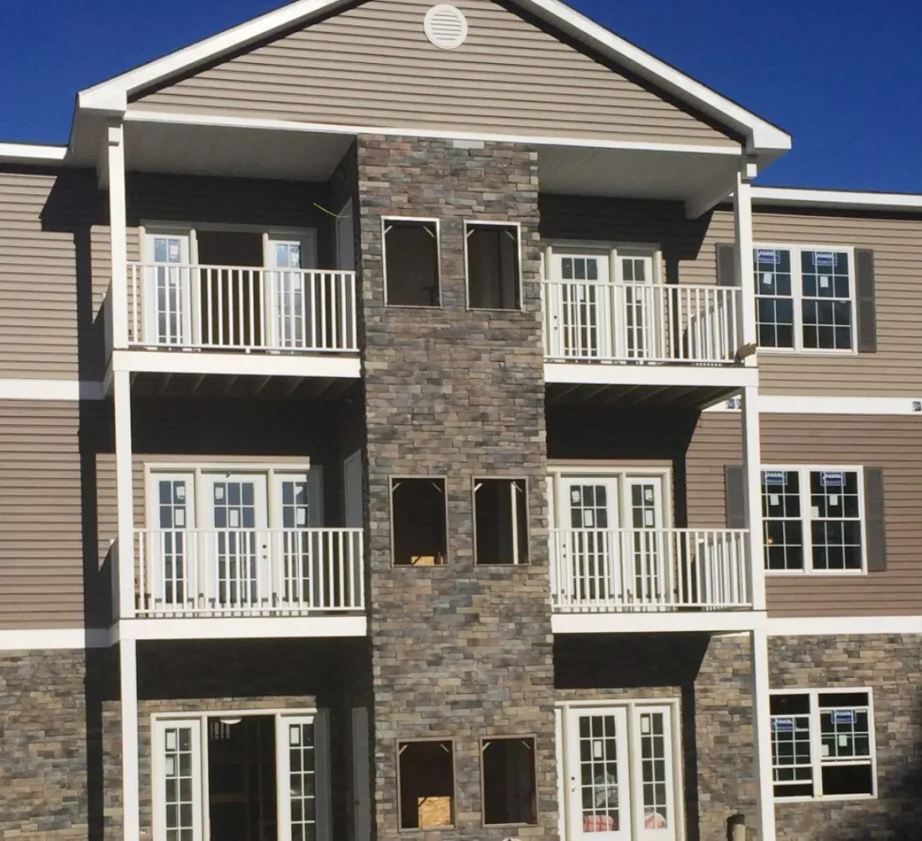 Three-story building with stone and siding exterior, featuring balconies and large windows.