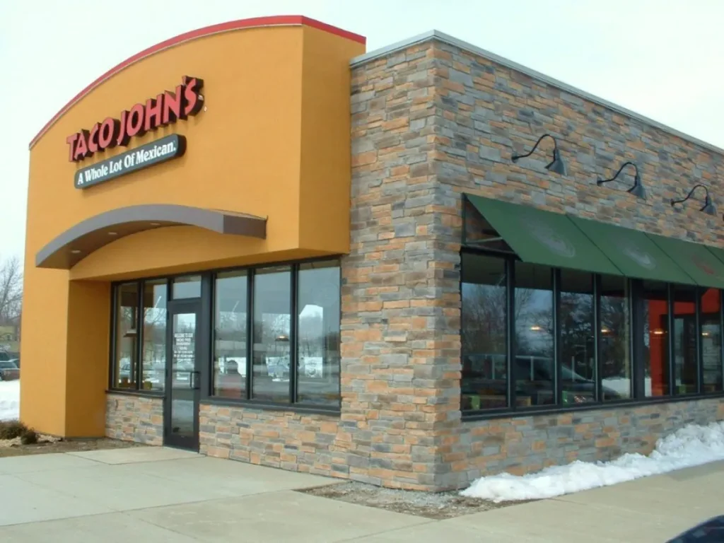 Taco John’s restaurant building with stone and yellow walls, large windows, and snow on the ground outside.