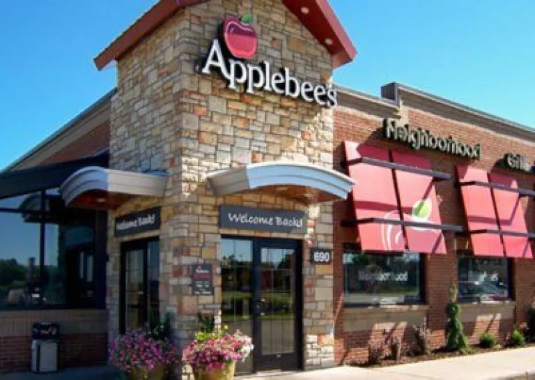 Applebee’s restaurant exterior with stone facade, red awnings, and plants by the entrance on a sunny day.