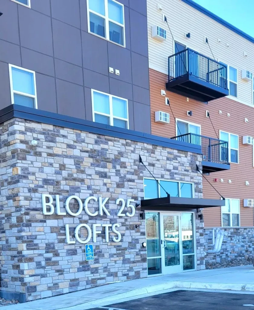 Block 25 Lofts building entrance with stone facade, glass doors, and accessible parking sign in front.