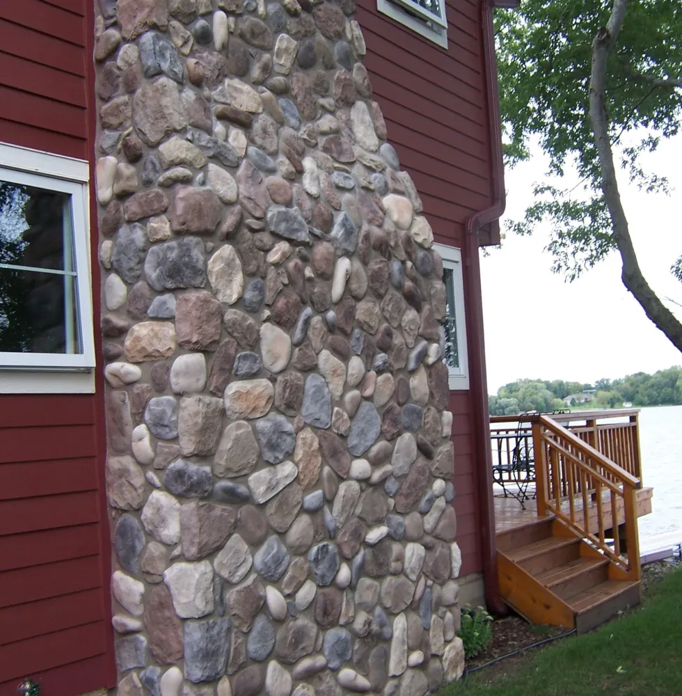 country-1 Stone chimney on red house beside wooden steps, with lake and trees visible in the background.