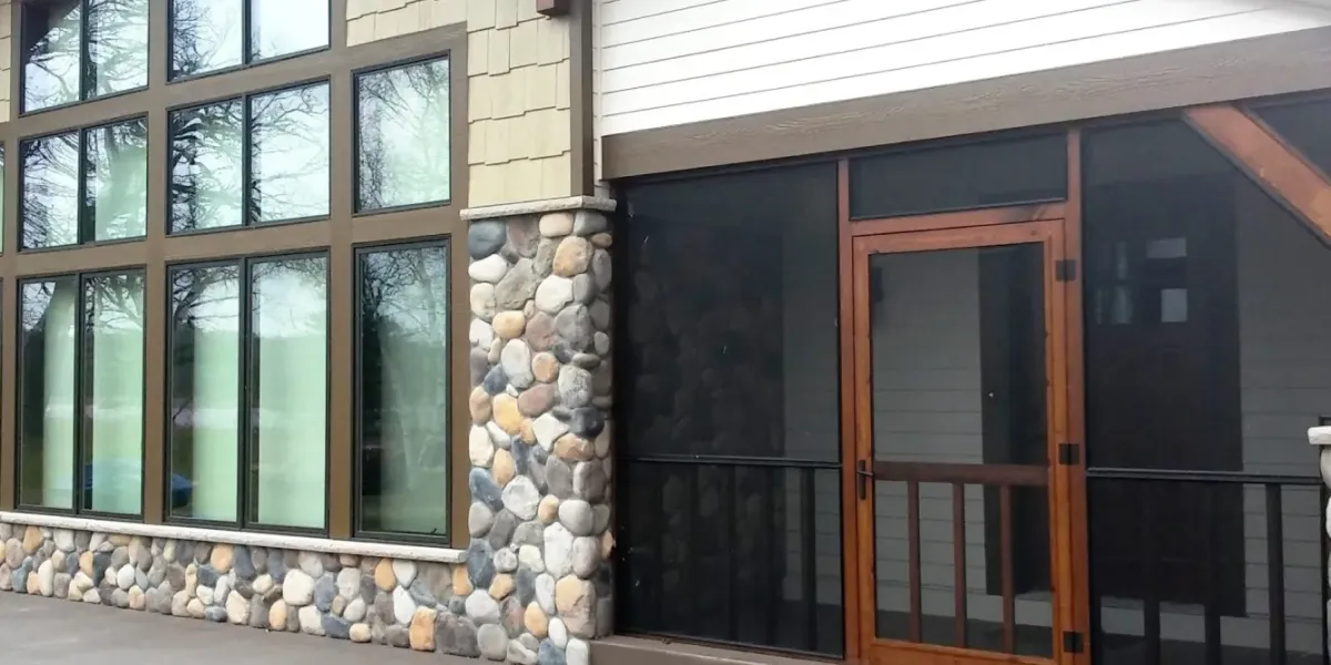 House exterior with large windows, stone wall, and a screened porch with a wooden door.