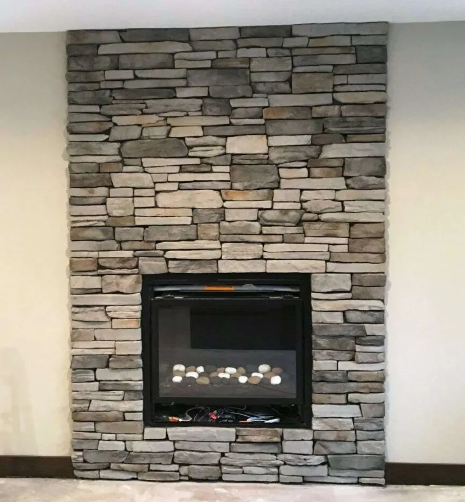 A modern fireplace set in a tall stone wall, with light and dark rectangular stones stacked neatly.