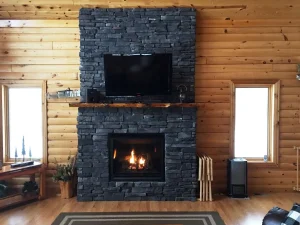 fireplace-4 Stone fireplace with a TV above it, set in a log cabin room with wood walls and two windows.