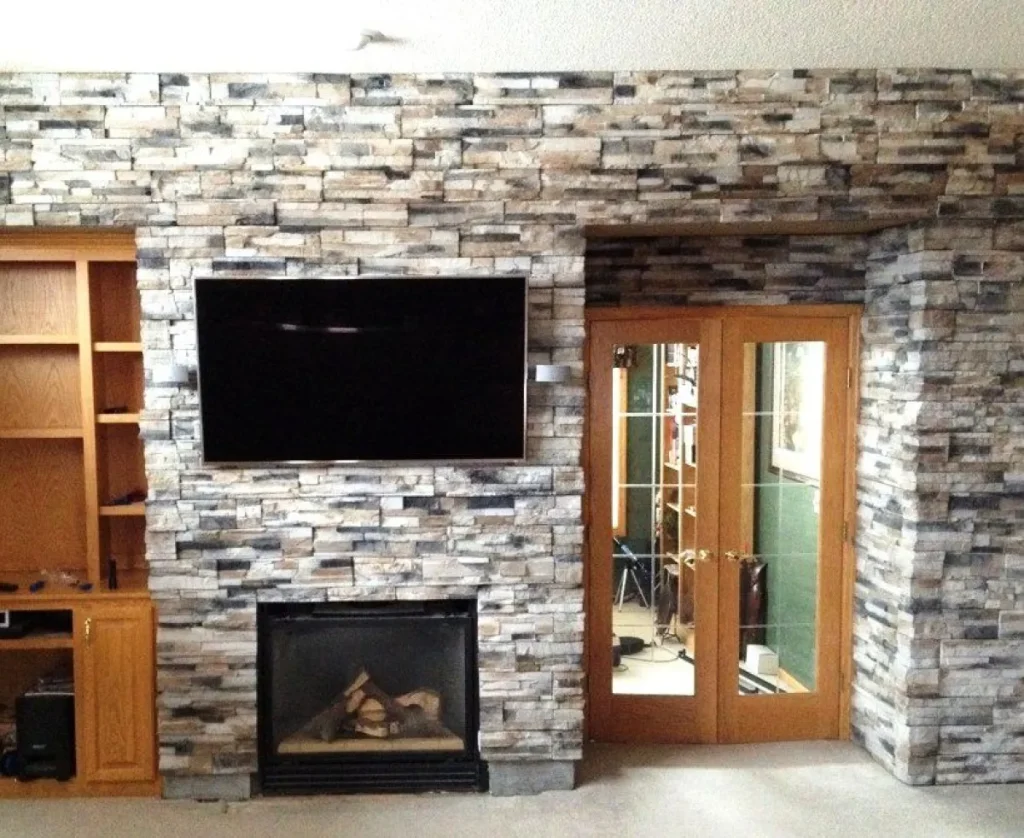 Stone wall with a mounted TV, fireplace below, wood shelves to the left, and glass double doors to the right.