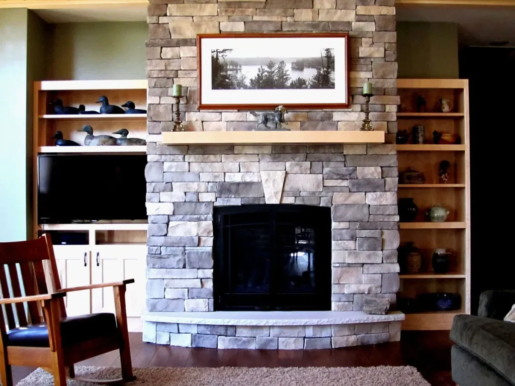 Stone fireplace with mantel, framed photo above, shelves on both sides, and a wooden chair in front.