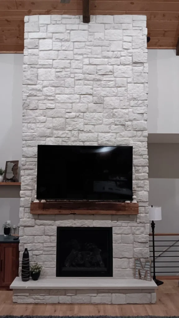 A stone fireplace with a TV mounted above and wooden mantel, in a modern living room.
