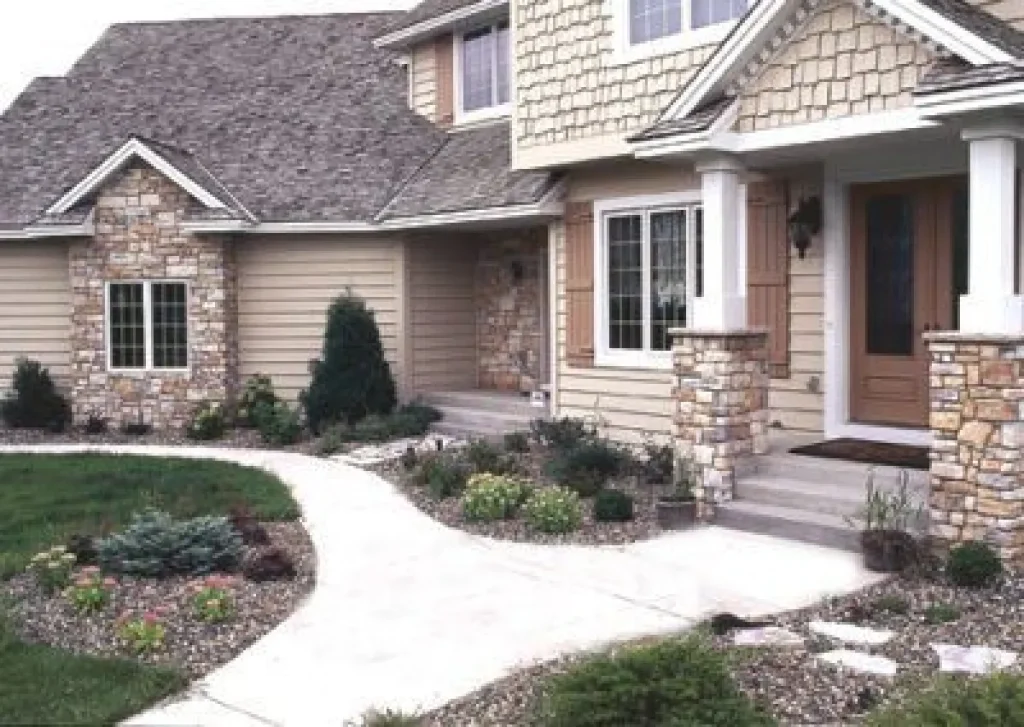 Stone and wood house exterior with a front porch, landscaping, and a curved sidewalk.