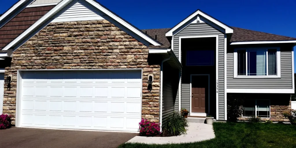 Modern suburban house with stone and siding exterior, white garage door, and a small front lawn.