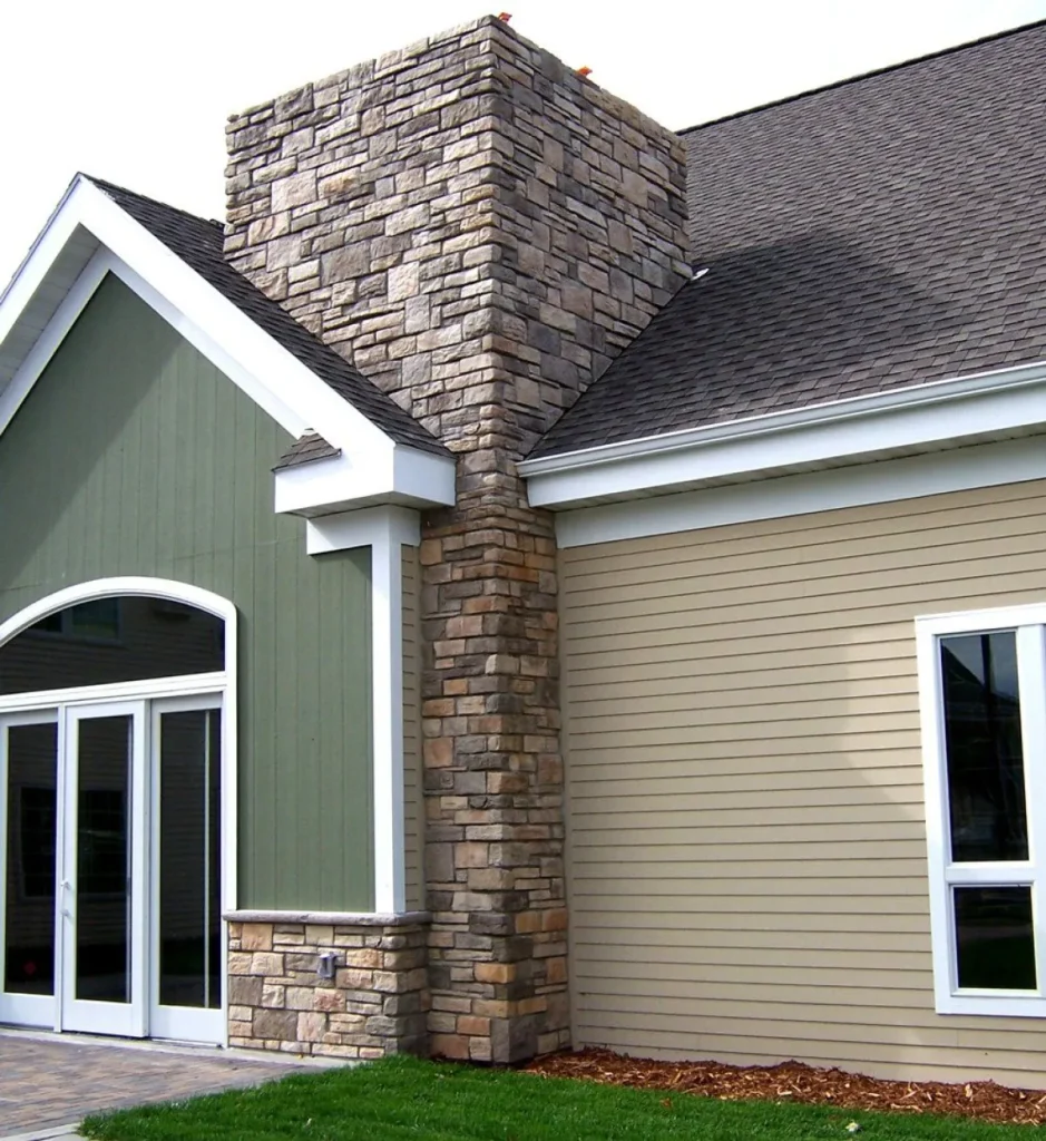 House exterior with green and tan siding, stone chimney, white trim, and large windows and doors.
