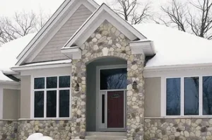 residential-2 Stone house with a red front door, snow on the roof, and bare trees in the background.