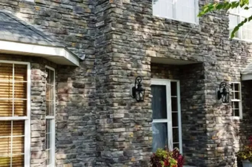 Two-story house with a stone exterior, white-framed windows, and a white door, surrounded by shrubs.
