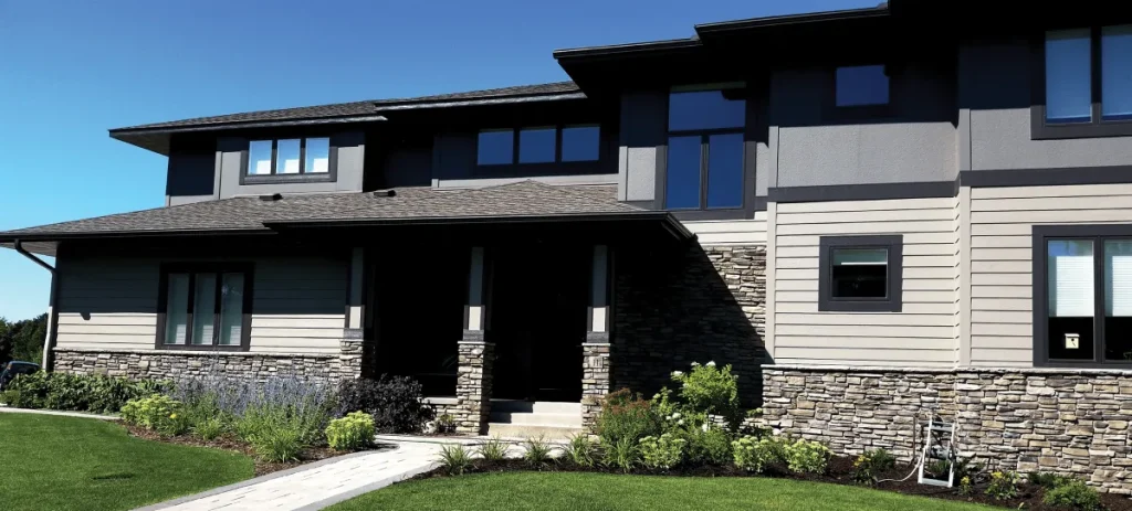 Modern two-story house with stone and siding exterior, dark trim, and landscaped front yard under blue sky.