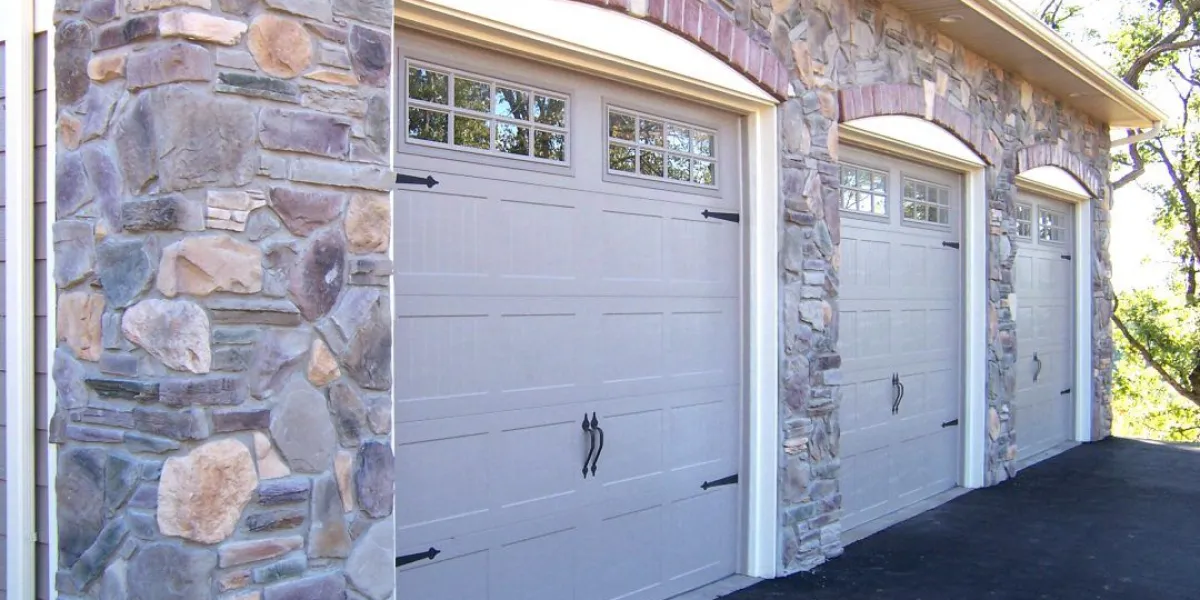 Three light gray garage doors with windows set in a stone facade; detail view of stonework on the left.
