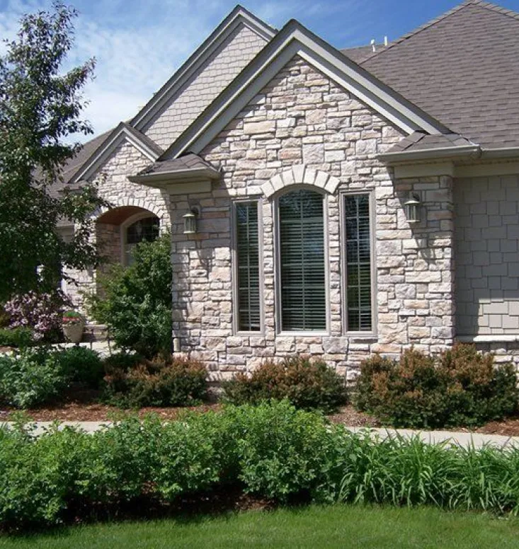 traditional-1 Stone house with large front window, green bushes, and a well-kept lawn under a blue sky.