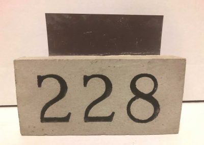 A rectangular block with the number 228 painted in black on its front, against a plain background.
