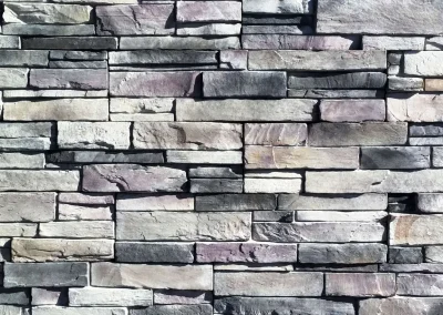 Gray and tan rectangular stone bricks stacked in an uneven, textured pattern on a wall.