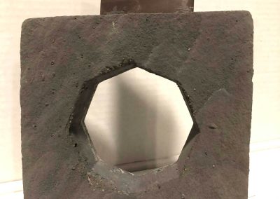 A rough, square stone with a hexagonal hole and a rectangular metal plate at the top.