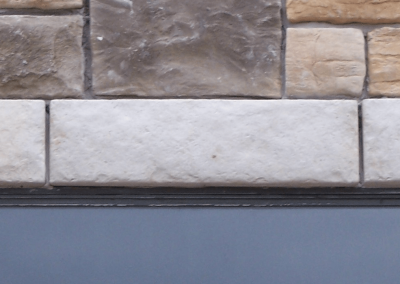 Stone wall with a rectangular window below three large gray stones, surrounded by tan and brown stones.