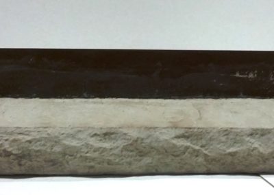 A rectangular stone slab placed in front of a straight black metal ruler on a white surface.