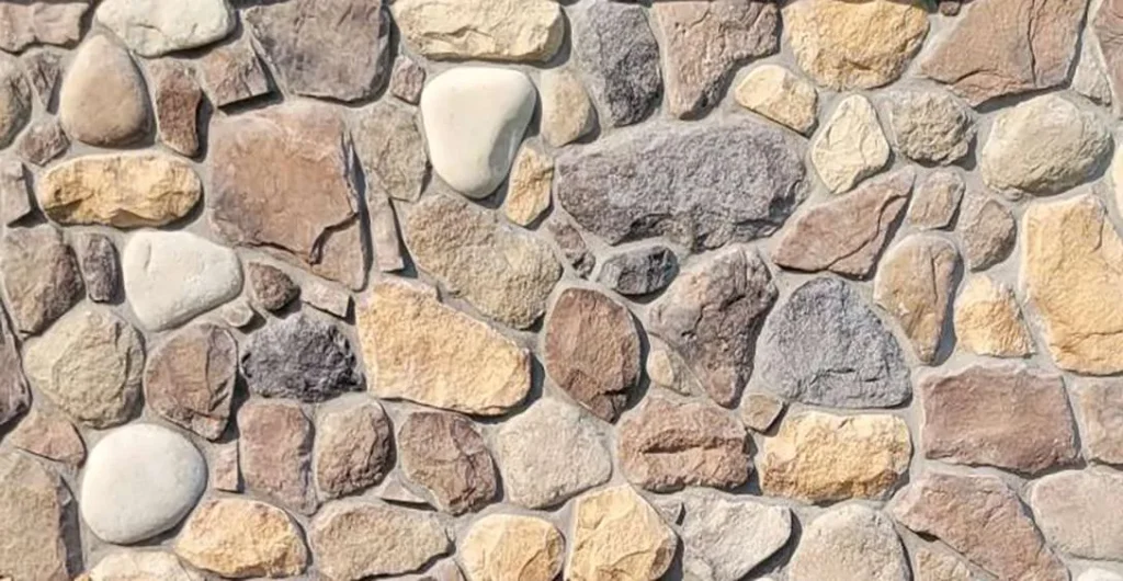 Alexandria-Stone A close-up of a stone wall with variously sized and colored rocks set in mortar.