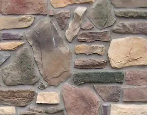 Various shapes and colors of stones fitted together in a decorative masonry wall.