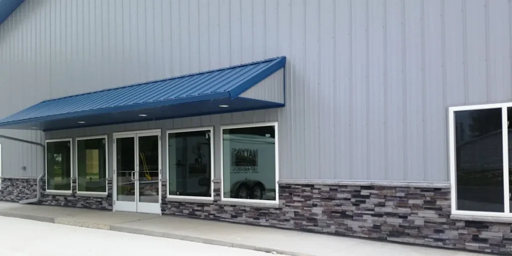 Gray metal building with large windows, stone accent, and blue metal awning above the entrance.