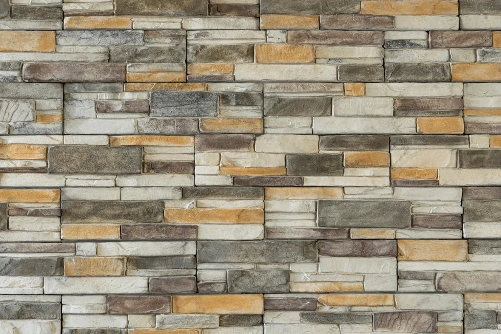 Patterned stone wall with rectangular gray, beige, brown, and tan bricks in a horizontal arrangement.