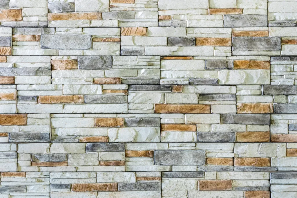 A wall made of rectangular gray, beige, and white stone bricks arranged in a horizontal pattern.