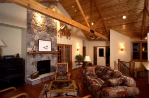 Cozy living room with a stone fireplace, wooden beams, patterned sofa, and animal decor on the mantle.