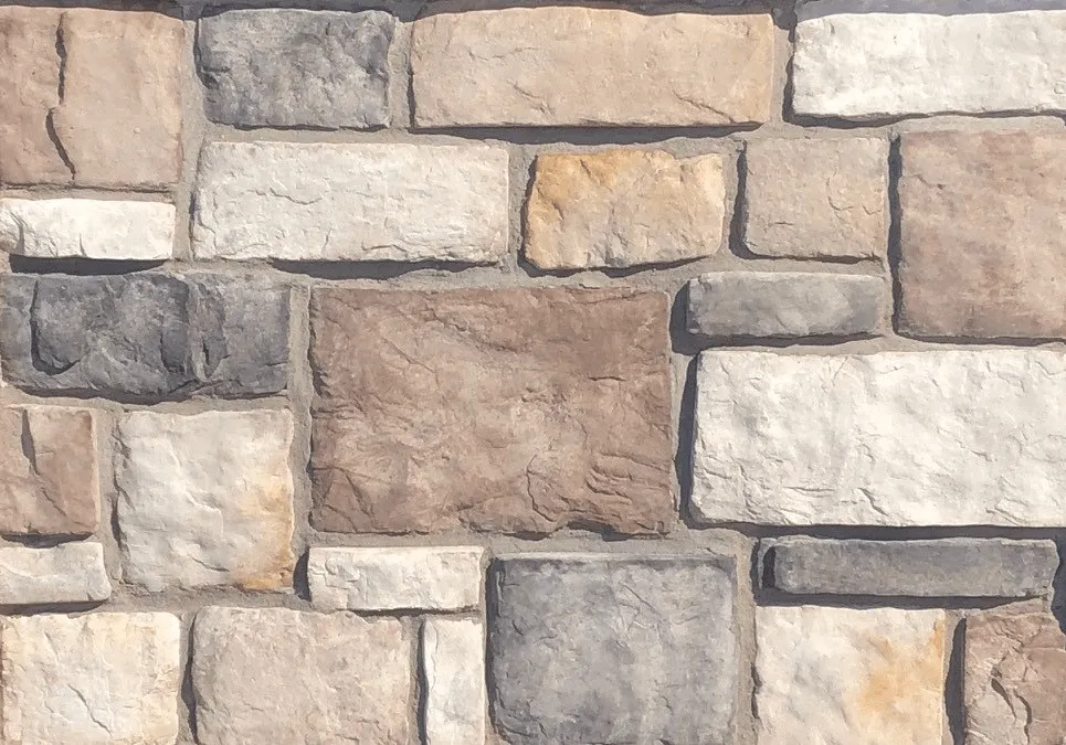 Hackett-Yukon A wall made of rectangular stones in various shades of beige, gray, and brown, arranged in a pattern.