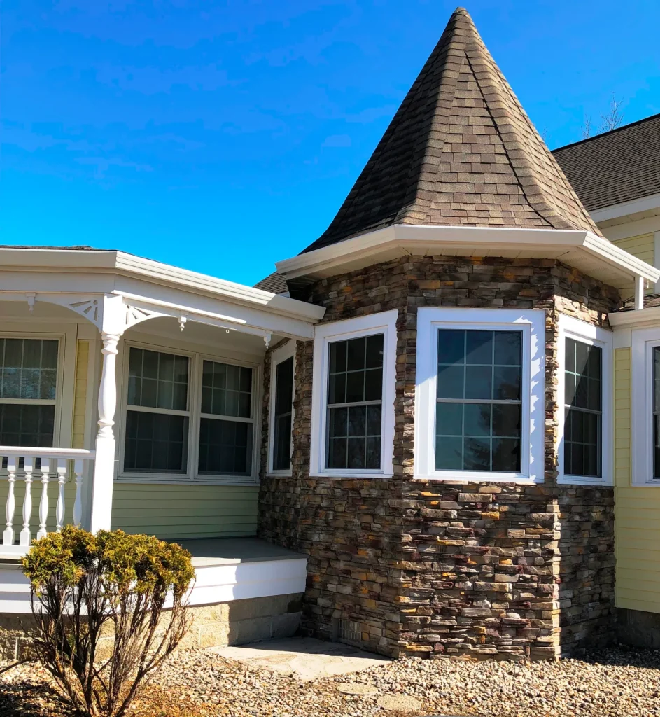 A house with a stone turret, large windows, white trim, and a covered porch with columns.