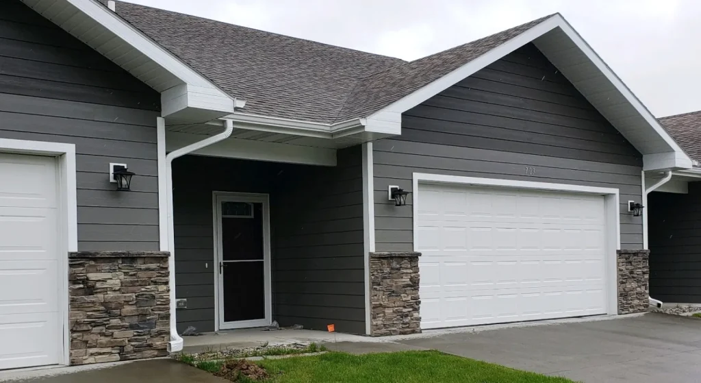 Gray house with stone accents, white trim, a double garage door, and a small lawn in front.