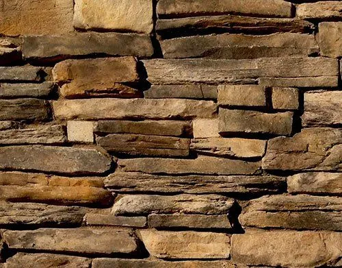 Close-up of a stone wall with uneven, stacked rectangular rocks in various shades of brown and tan.