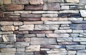 A close-up of a stone brick wall with various shades of beige, gray, and brown stacked horizontally.