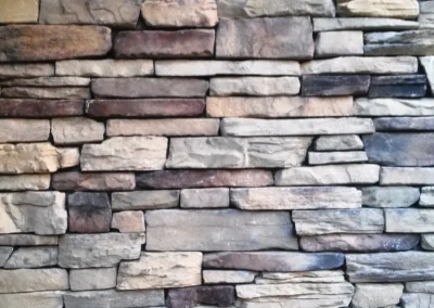 A close-up of a stone brick wall with various shades of beige, gray, and brown stacked horizontally.