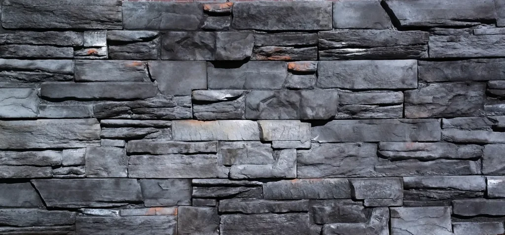 Gray stacked stone wall with rough, irregular rectangular stones and slight hints of orange-brown areas.