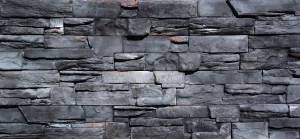 Gray stacked stone wall with rough, irregular rectangular stones and slight hints of orange-brown areas.