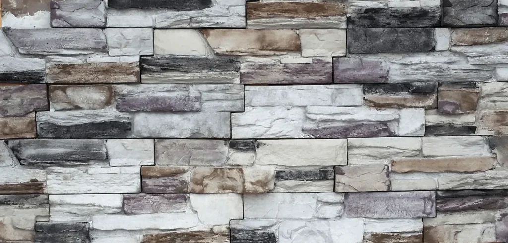 Stacked stone wall with rectangular blocks in shades of gray, brown, and beige, arranged in rows.