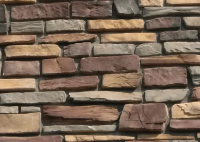 A wall made of rectangular stones in various shades of brown, tan, and gray, stacked unevenly.