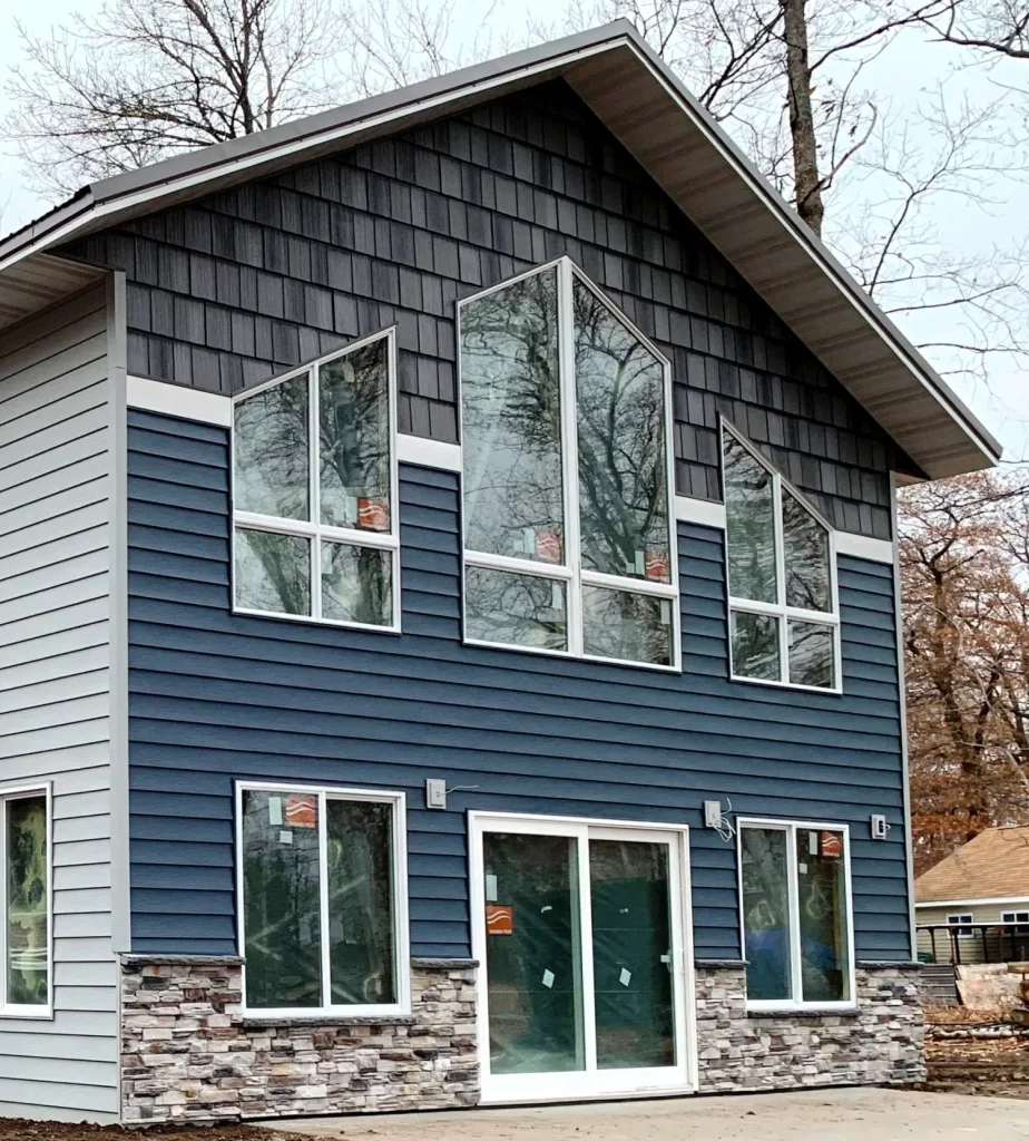 Modern two-story house with blue and gray siding, stone accents, and large geometric windows.