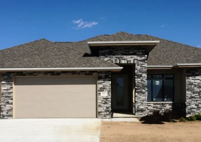 Single-story house with stone exterior, two-car garage, and new landscaping under a clear blue sky.