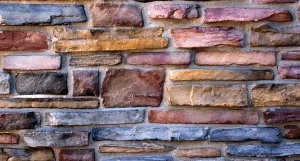 Close-up of a multicolored stone brick wall with various shades of brown, gray, and red bricks.