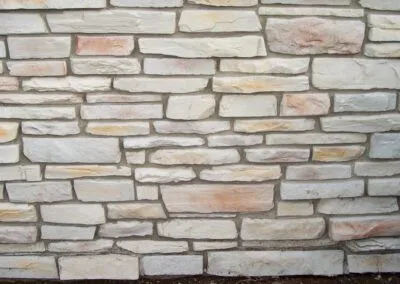 Prairie-Ledgestone-Custom-Colonial-Sunny A close-up of a stone wall made of rectangular, light-colored stones with uneven sizes and shapes.