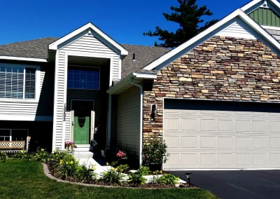Two-story suburban house with stone and siding, green front door, and double garage on sunny day.