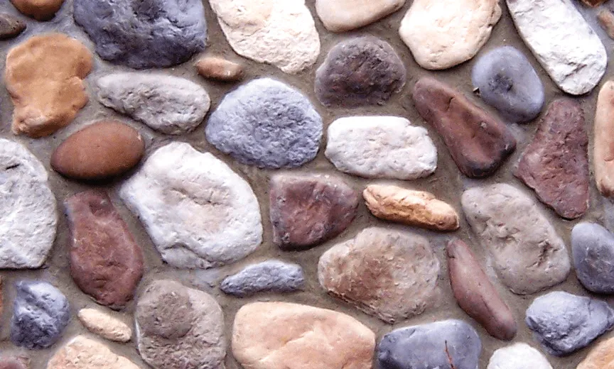 River-Rock A close-up of a stone wall with variously colored and shaped stones set in gray mortar.