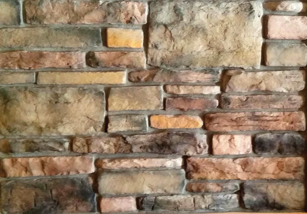 Weatherledge – Mountain Moss A close-up view of a textured stone brick wall with various shades of brown and tan bricks.