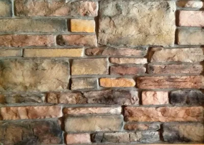 A close-up view of a textured stone brick wall with various shades of brown and tan bricks.